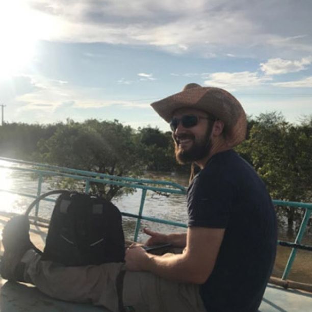 一本道Education student Connor Wolf smiling and sitting on a boat as he tours a lake in Cambodia. 