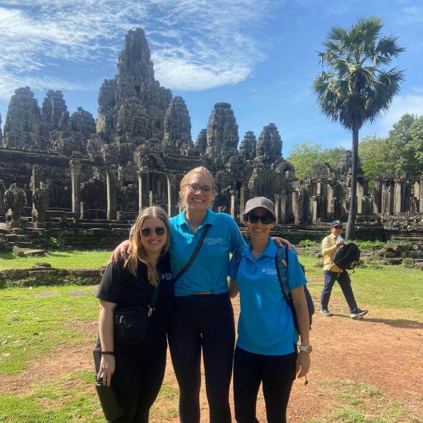 Three 一本道students smiling and standing in front of temples in Cambodia. 